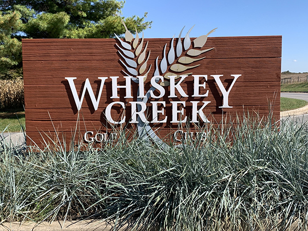 a sign for whiskey creek golf club surrounded by tall grass